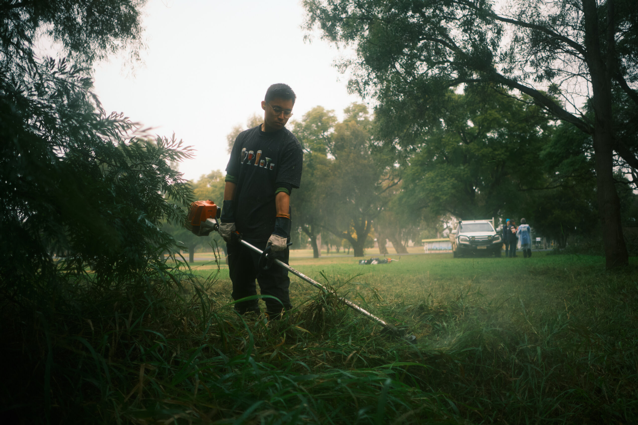 A man holding a lawn trimmer, trimming some grass.